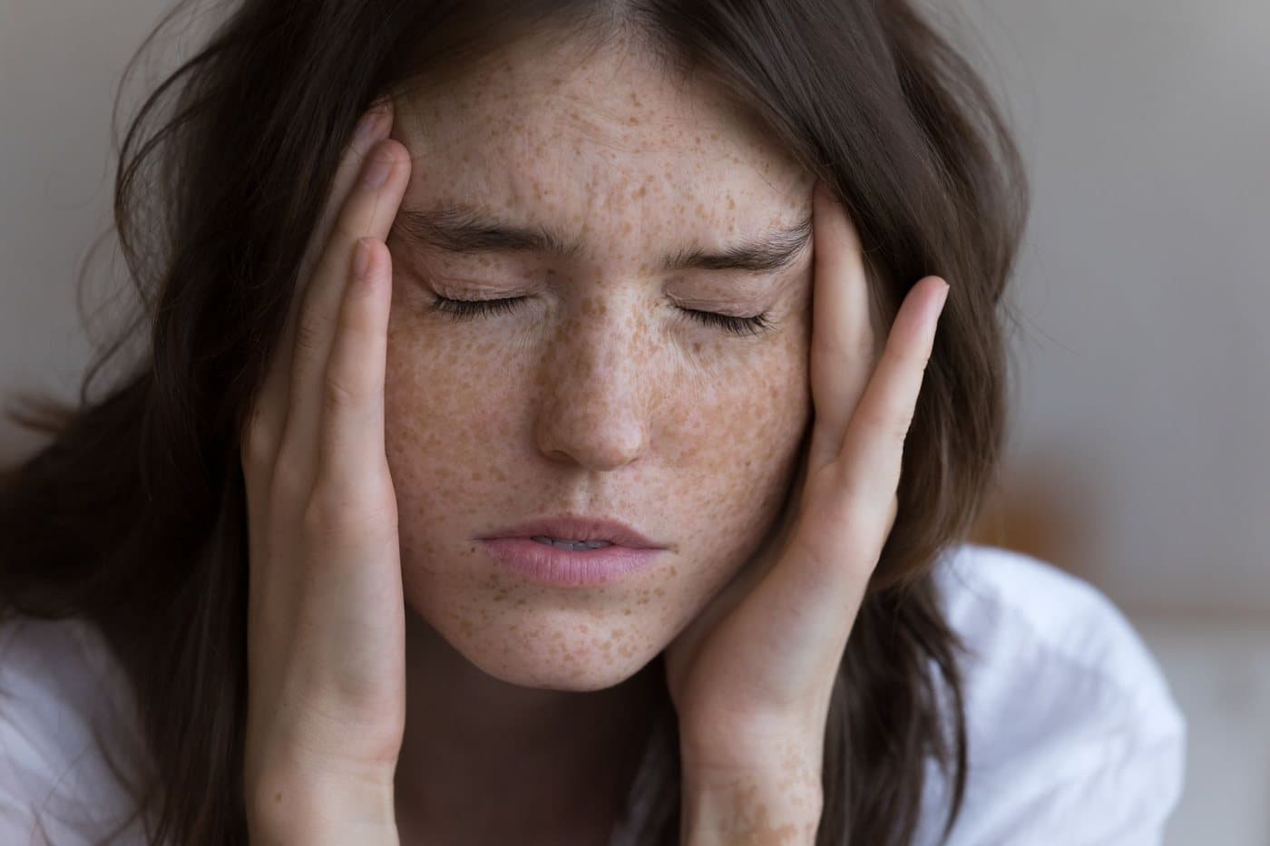A woman with her eyes closed resting a hand against her temple, worn out