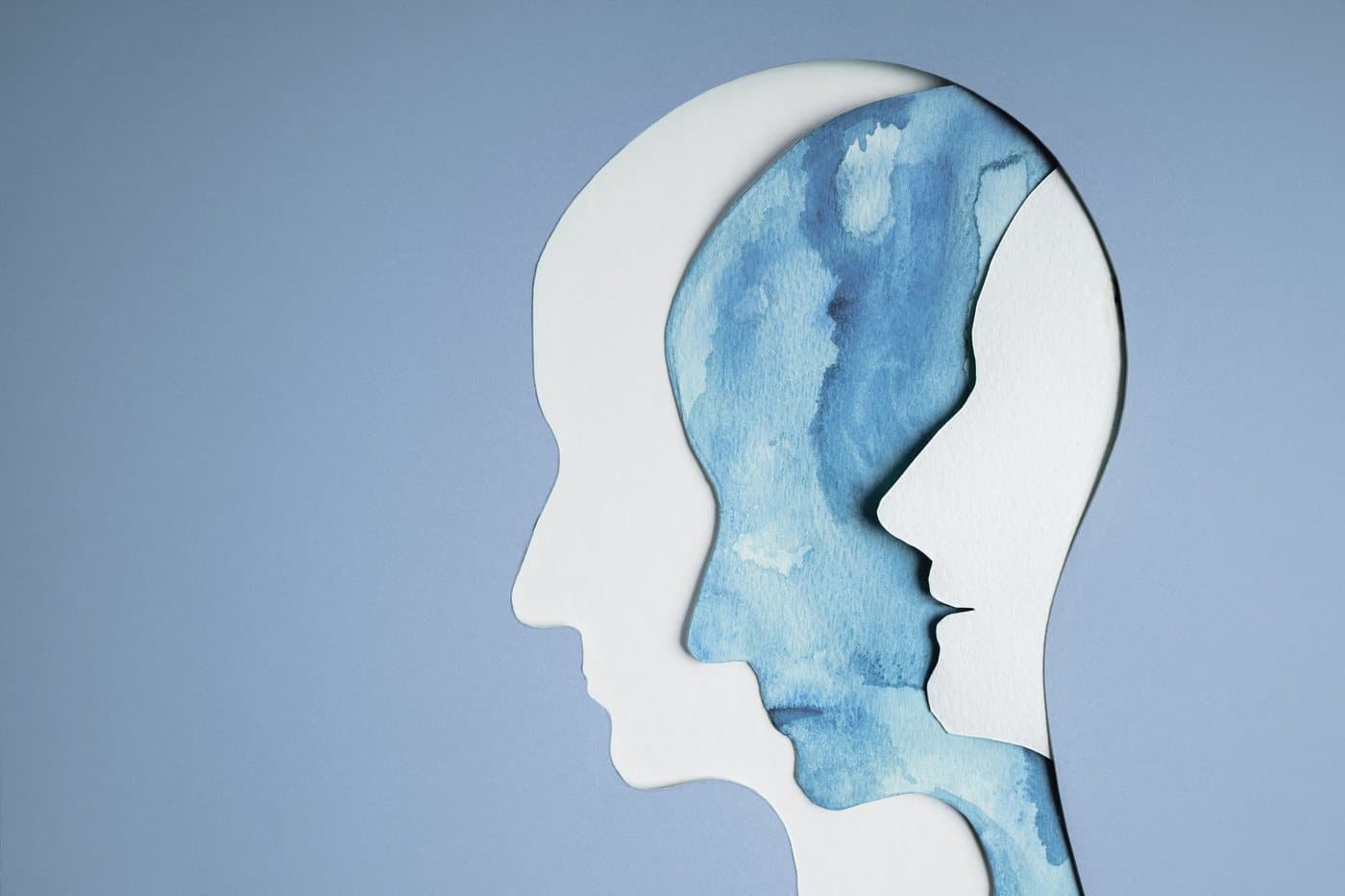 Two paper cut head profiles in blue watercolour, one nested inside the other