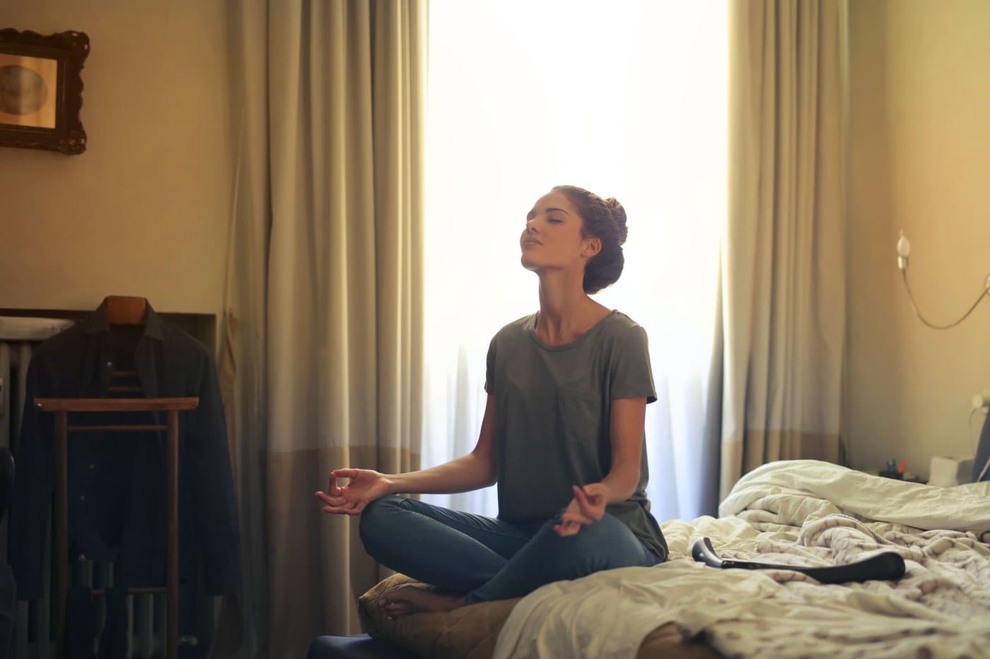 A person sitting cross legged on a bed in morning light