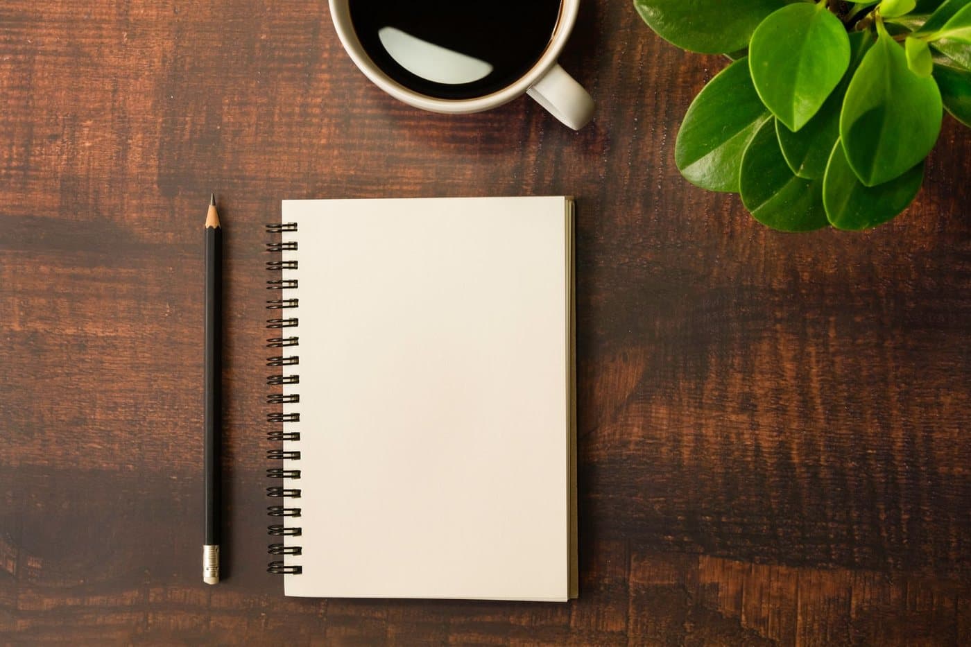 An open notebook with a pencil and a cup of coffee on a wooden desk