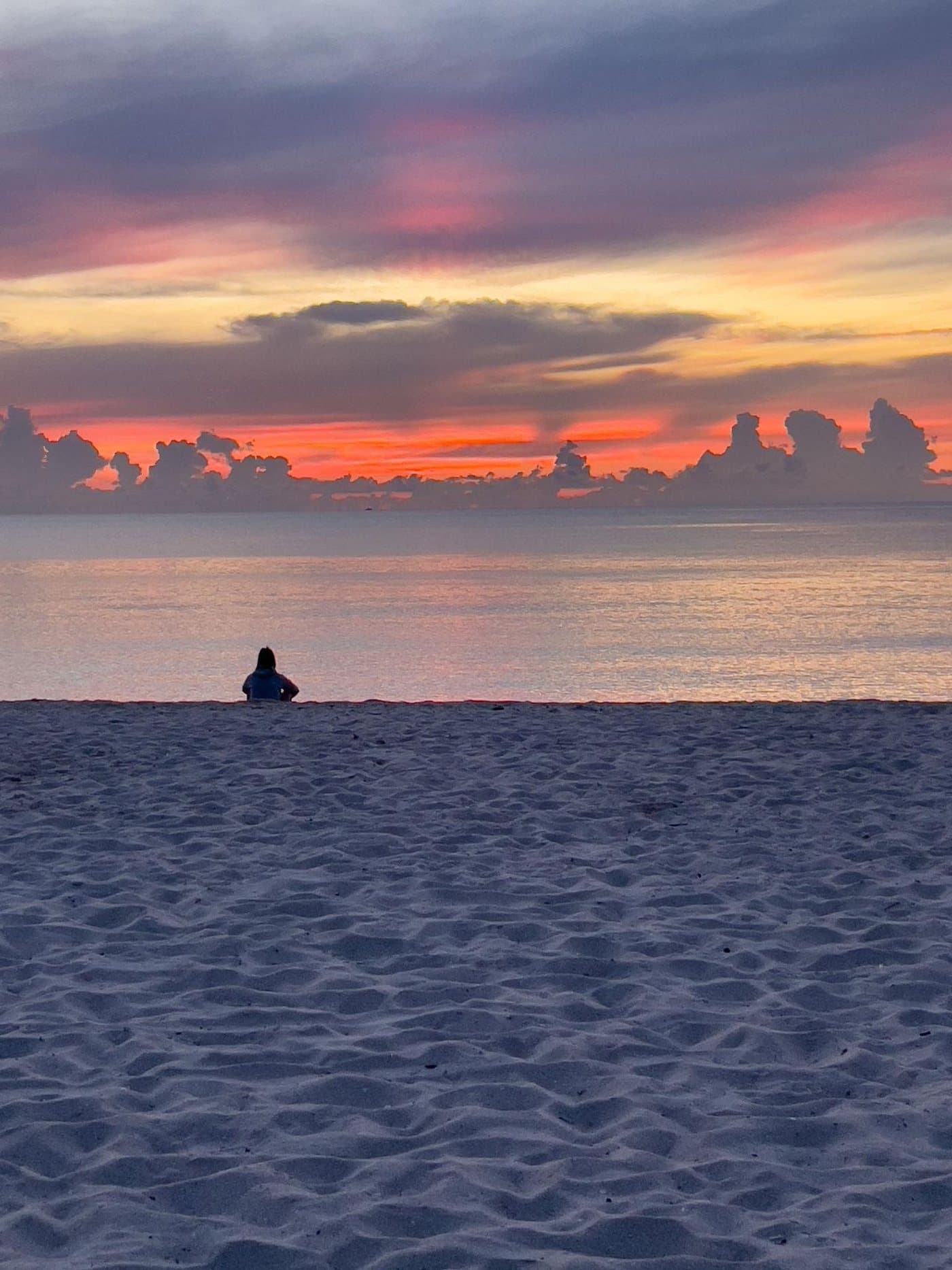A lone figure on a wide beach at sunset