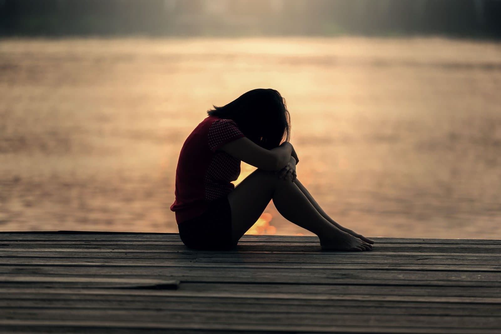 Person sitting alone on a dock at sunset