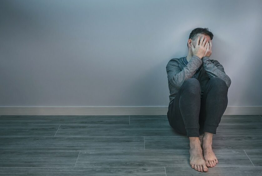 Unrecognizable man with problems crying while covering his face with hands sitting on the floor